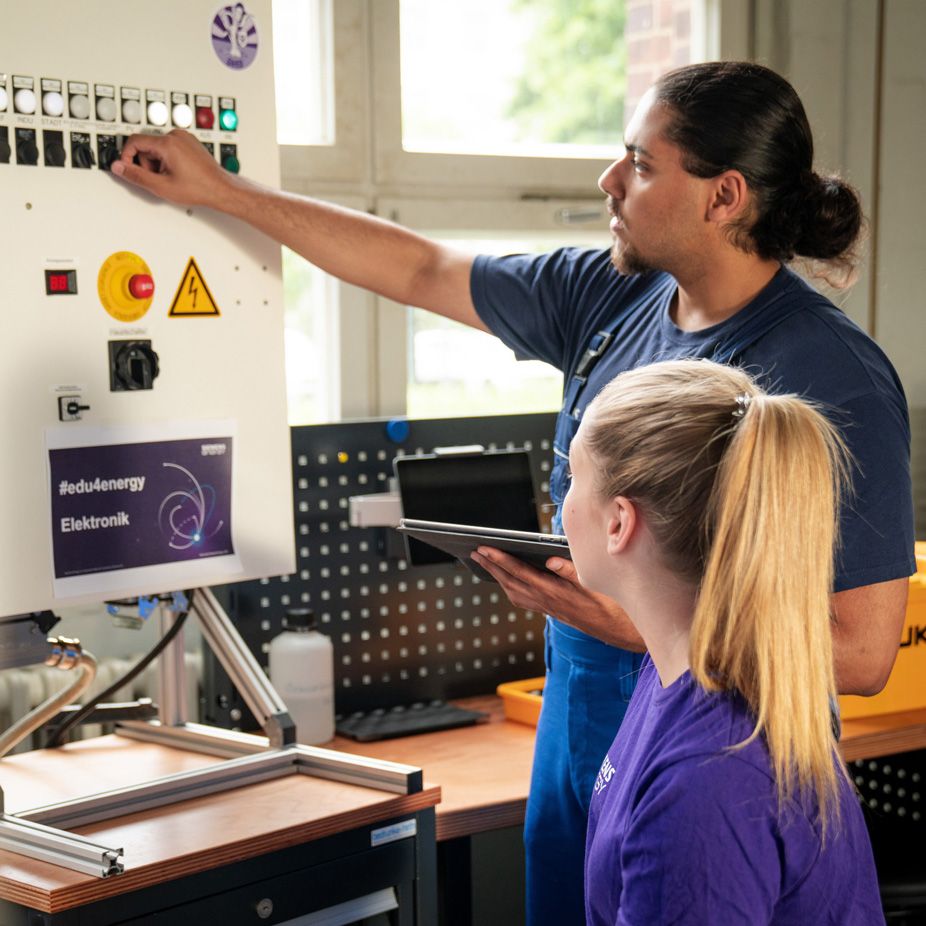 Two apprentices of Siemens Energy operate a control box.