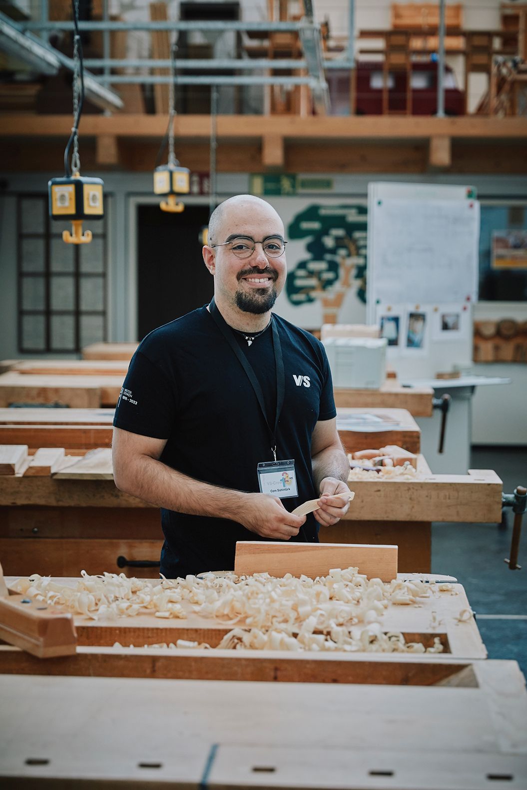 A man stands at a workbench in the wood workshop of VS and smiles at the camera.