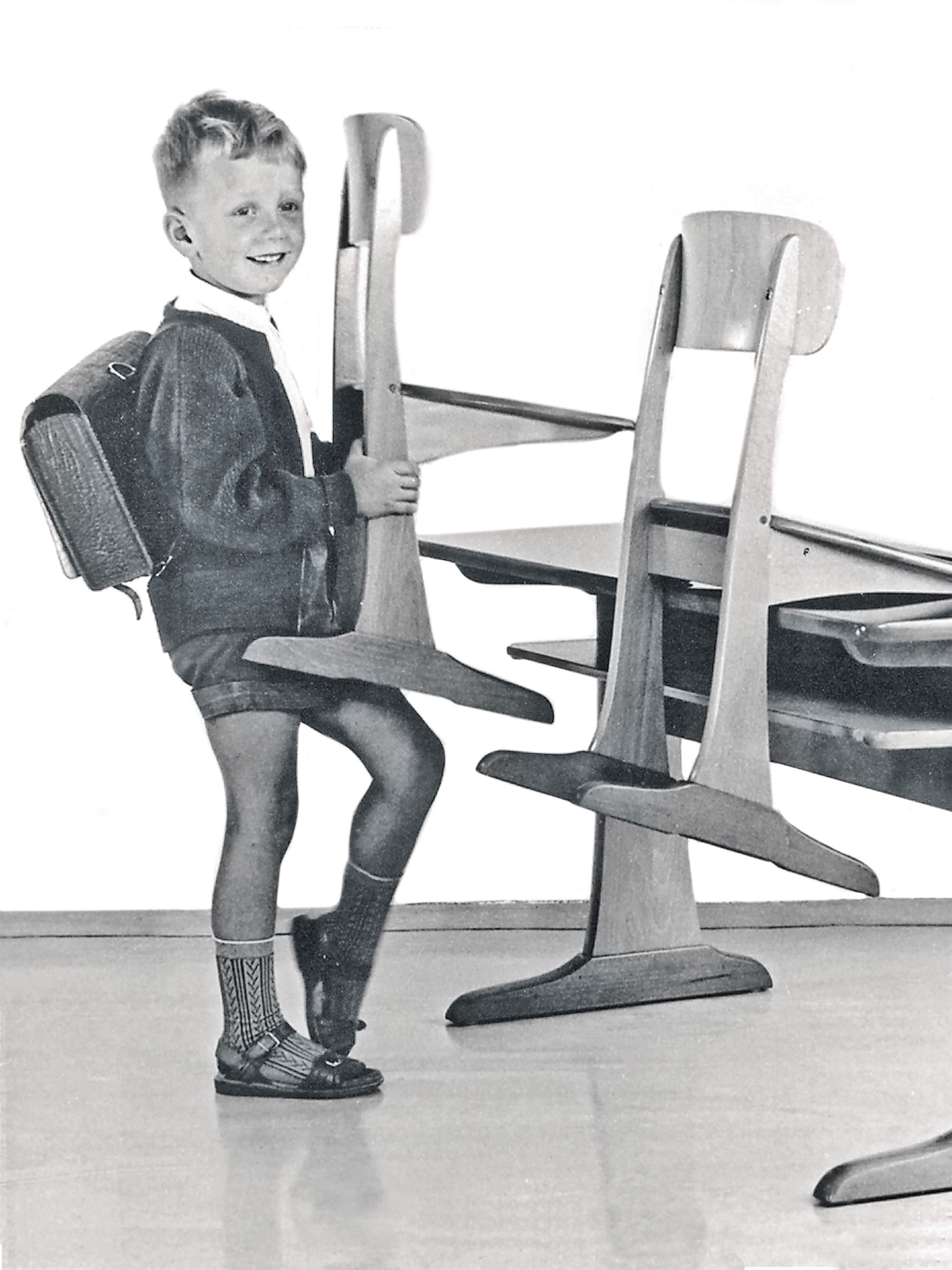 Schwarz-Weiß-Bild von einem Jungen, der einen VS Kufenstuhl aus Holz auf einen Kufentisch aufstuhlt.