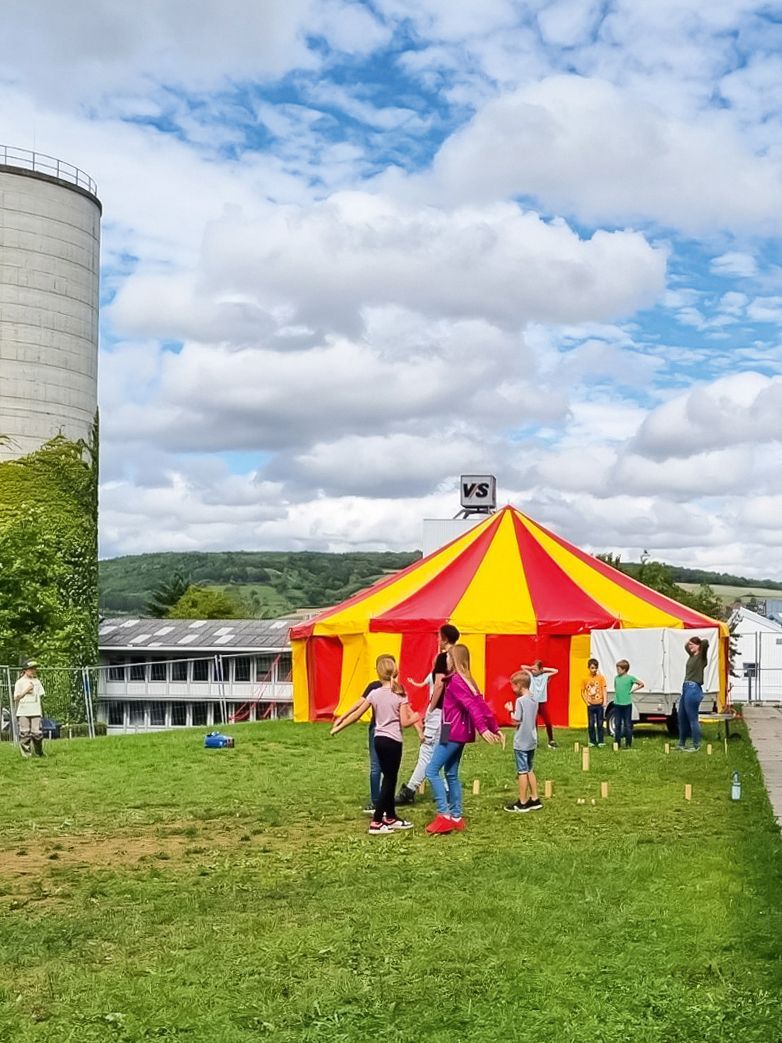 Kinder spielen vor einem Eventzelt bei der VS-Ferienbetreuung Holzwürmer