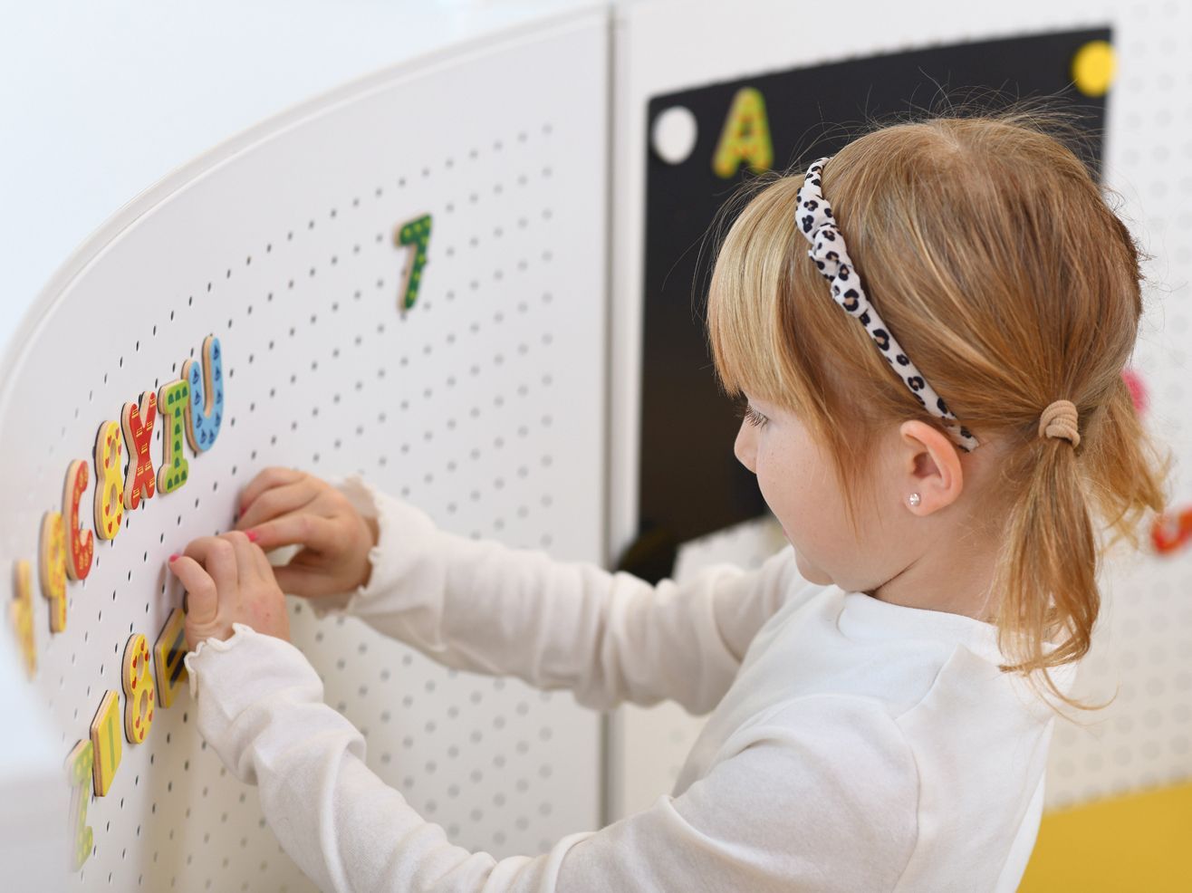 Ein Mädchen lernt mit magnetischen Buchstaben und Zahlen an einer Lochwand.