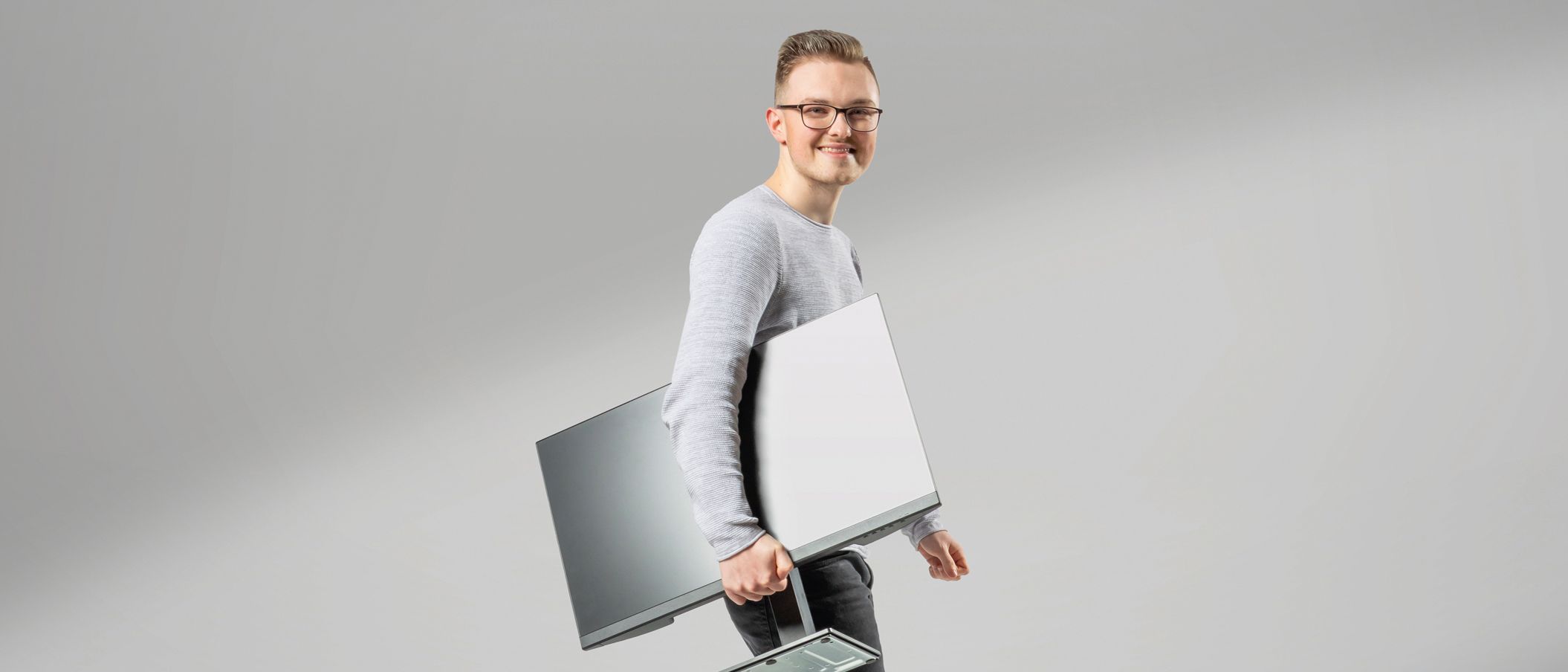 A young computer science student with a screen under his arm smiles at the camera